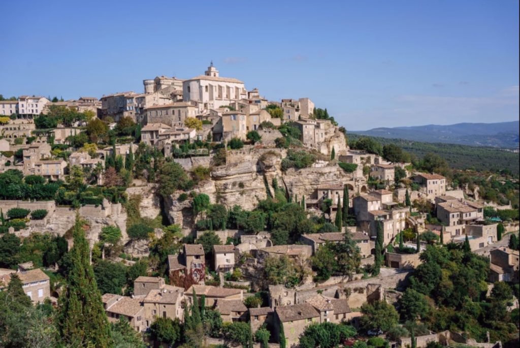 Hillside Provençal town. Old buildings wrap around this hillside with tress dotted between them.