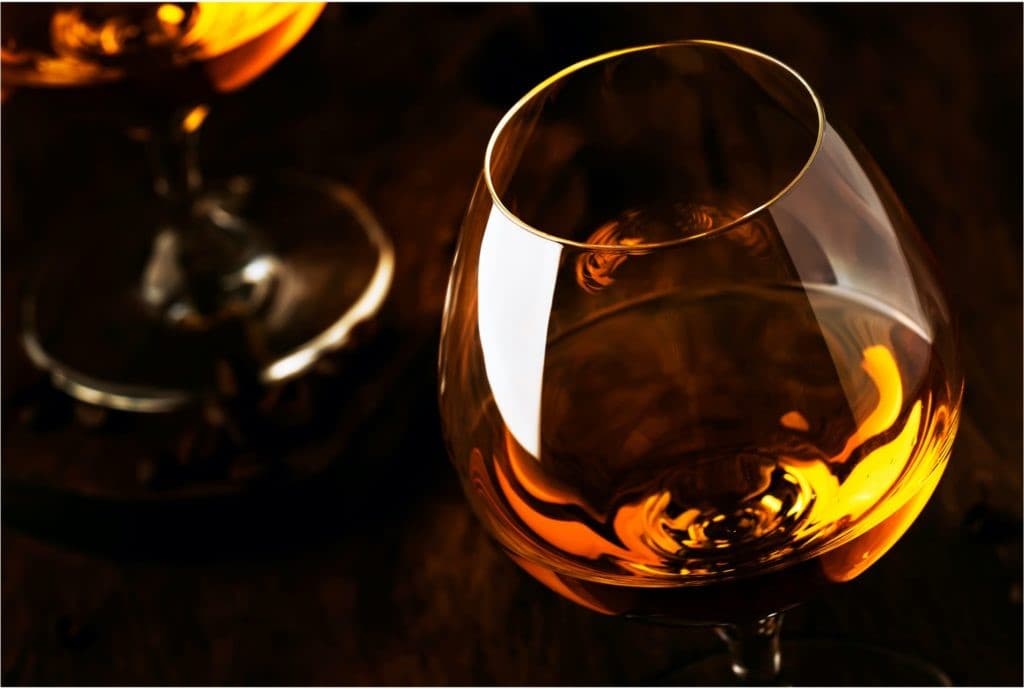 A brandy glass filled about 1/3 of the way with Cognac brandy. The spirit is a rich amber colour in the glass
